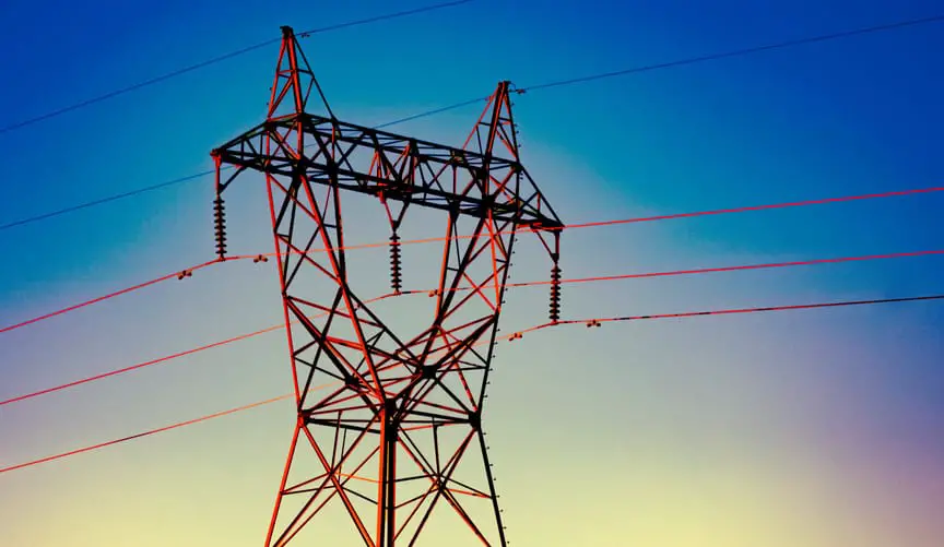 Electric power transmission tower silhouetted against a colorful sunset sky, with high-voltage power lines extending from the tower.